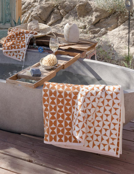 #color::sudan-brown-moon | The Harper orange and white towel by house number 23 with half-moon designs is hung on a stone bathtub in an outdoor space
