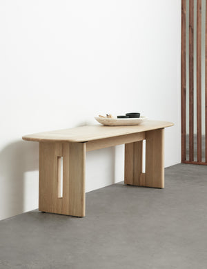 The Henrik light wood bench sits against a wall with a narrow wooden bowl sitting atop of it