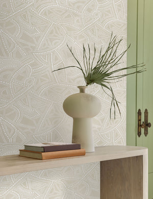 The Heritage light neutral-toned Wallpaper with a carved and etched pattern by Malene Barnett is in a room with green french doors, a sculptural ceramic vase, and a wooden side table