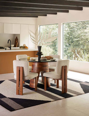The hidara rugs lays in a dining room attached to a kitchen under a round dining table and four cream boucle dining chairs
