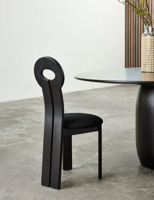 The Whit black wood sculptural dining chair by sarah sherman samuel sits in a room next to a circular black wood dining table with a jute wrapped glass vase sitting atop it.