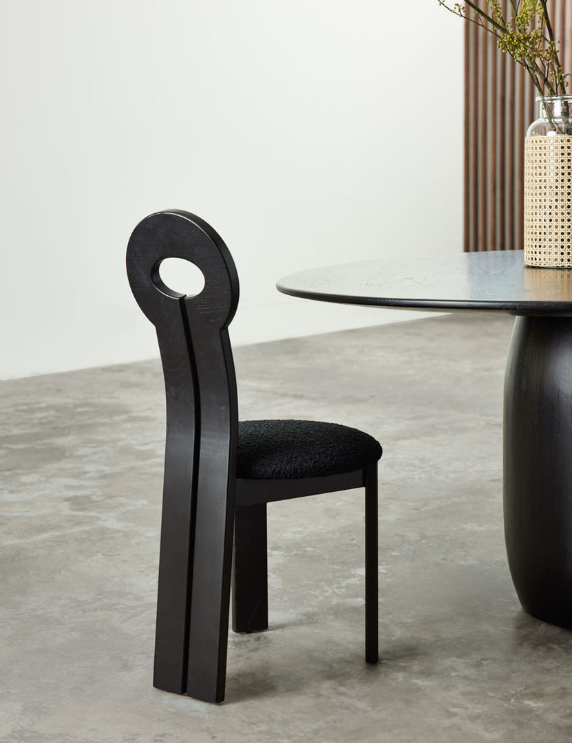 #color::black | The Whit black wood sculptural dining chair by sarah sherman samuel sits in a room next to a circular black wood dining table with a jute wrapped glass vase sitting atop it.