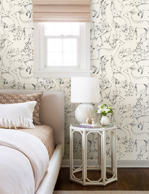 The Woodland Wallpaper is in a bedroom with a natural linen framed bed, an octagonal side table, and a rounded stone lamp