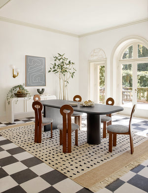 The whit honey wood sculptural dining chair by sarah sherman samuel sits in a bright dining room surrounding a black rectangular dining table atop of a polka dotted rug.