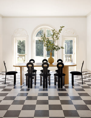 The Whit black wood sculptural dining chair by sarah sherman samuel sits in a bright dining room surrounding a natural wood dining table atop a black and white checkered floor.
