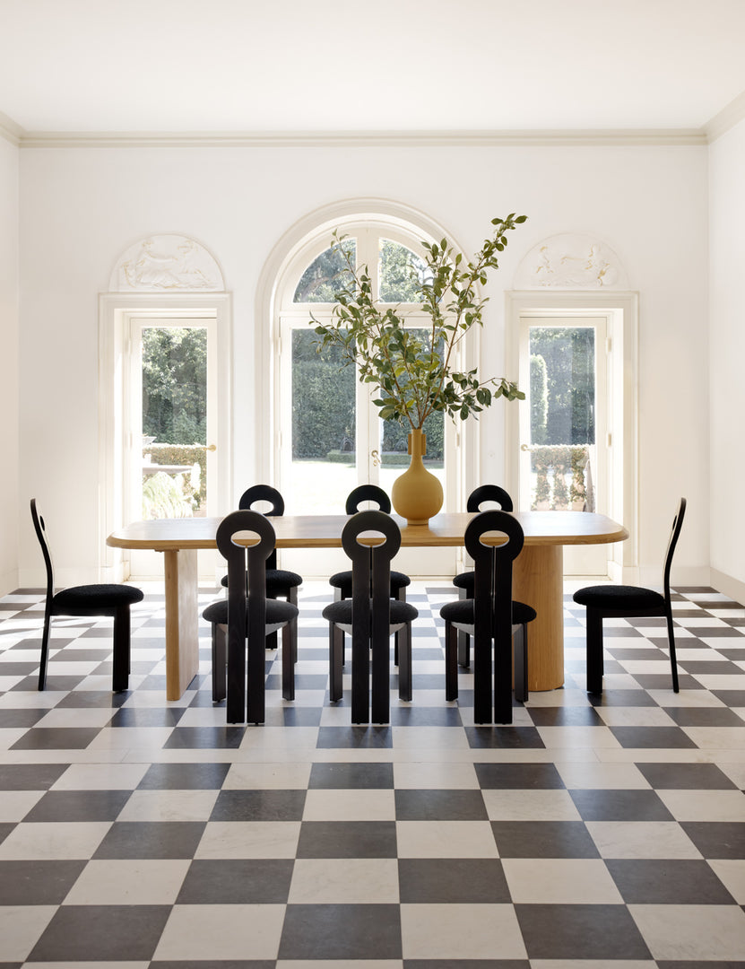 #color::black | The Whit black wood sculptural dining chair by sarah sherman samuel sits in a bright dining room surrounding a natural wood dining table atop a black and white checkered floor.