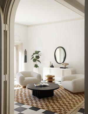 Two Billow ivory boucle lounge chairs sit atop an ochre ivory checkerboard rug with a black circular coffee table in between