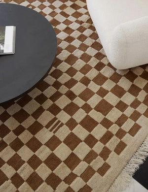 Bird’s-eye view of the Irregular ochre checkerboard rug by Sarah Sherman Samuel with a linen rounded accent chair and a black wooden coffee table