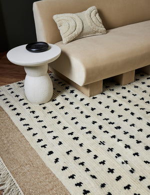 The irregular dots rug lays in a living room under a beige velvet armless sofa and a white sculptural side table