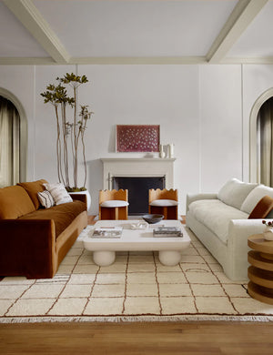 Ivory and ochre Irregular Grid Rug by Sarah Sherman Samuel lays in a living room in between a cognac velvet and linen sofa with a rounded coffee table in the middle