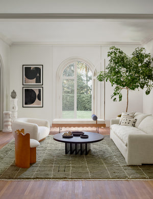 The Rupert natural linen sofa sits atop an olive green rug across from a round coffee table and a boucle accent chair