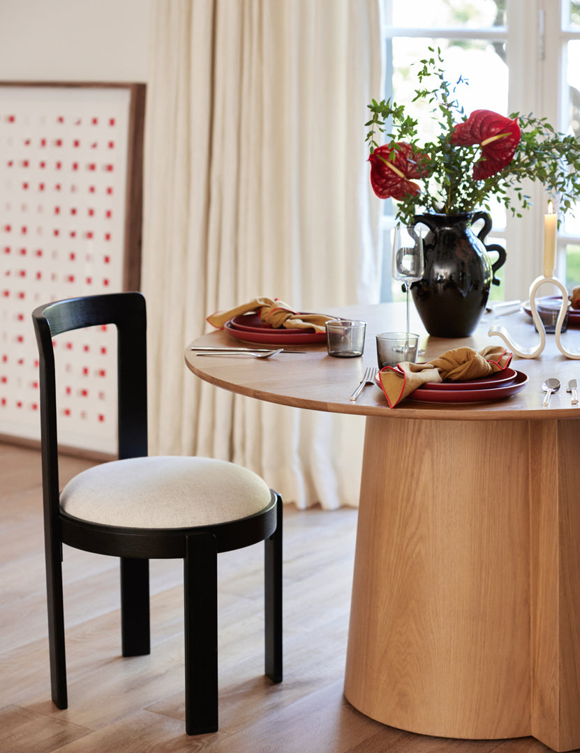 #color::natural #size::48- | The Pau oak veneer round dining table is fully set with red serveware and mustard linens next to a black dining chair