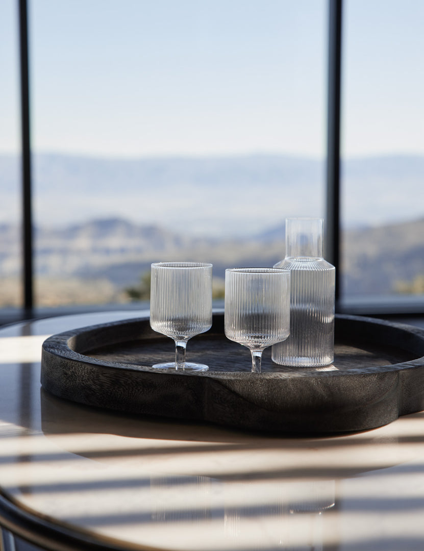 | The rian ripple wine glasses sit inside a black wooden tray with a rian ripple water carafe atop the thomas bina oval coffee table