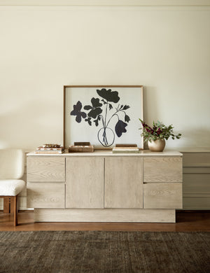 The Anemone floral navy and white wall artwork print sits atop a white-washed wooden side table in a living room with a plush brown rug
