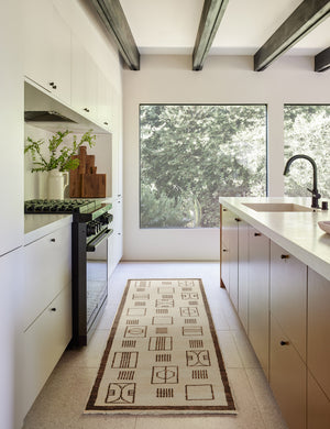 The jillian runner rug lays in a kitchen with black hardware, white cabinetry and countertops, and a wooden beamed ceiling