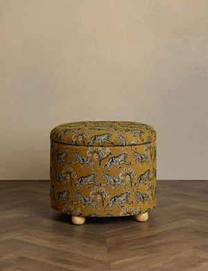 Kamila tiger golden round 24 inch ottoman with storage space and pinewood feet by Sarah Sherman Samuel sits in a studio room