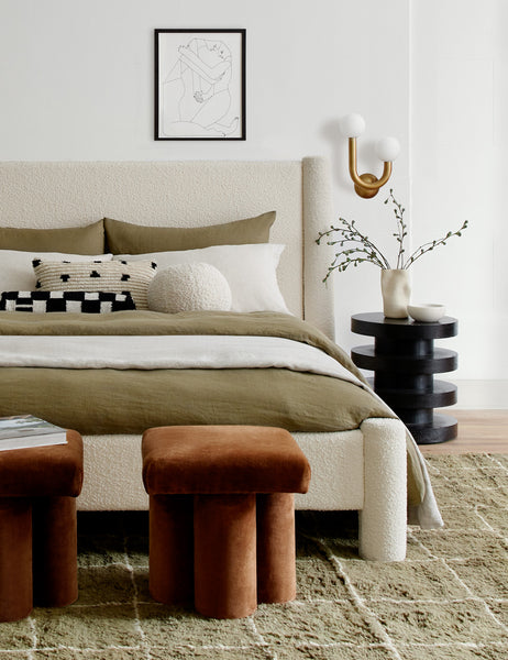 #color::ivory | Ivory Bouclé Ball Pillow by Sarah Sherman Samuel sits on a natural linen framed bed in a bedroom with a moss green rug and conganc ottomans