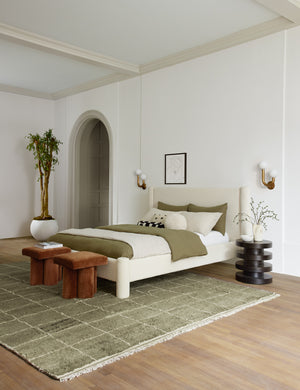 Ivory Boucle Hyvaa Bed sits in a bedroom with an olive rug, olive and cream linens, and two cognac velvet ottomans