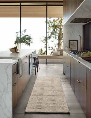 Dolan wool ivory rug in its runner size lays in a kitchen with wooden cabinetry and white marble countertops