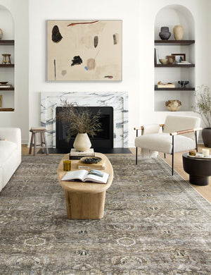 Amalia distressed traditional rug lays under an oval coffee table and boucle accent chair in a living room with a marble fireplace