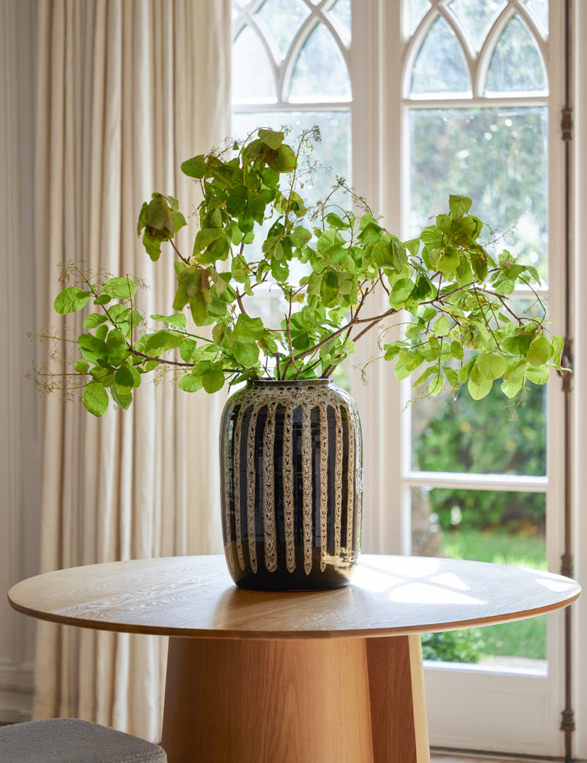 | Wheaton full-bodied black and natural striped vase with a plant inside sits on a round wooden dining table with french doors in the background