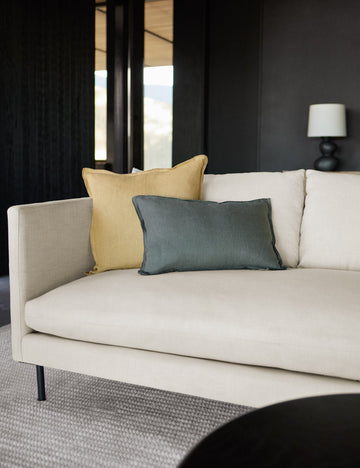 #color::conifer #style::lumbar #fill type::with-feather-down-insert #fill type::pillow-cover-only | The arlo conifer gray lumbar pillow sits on a natural linen sofa with a light yellow linen pillow