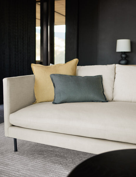 #color::conifer #style::lumbar | The arlo conifer gray lumbar pillow sits on a natural linen sofa with a light yellow linen pillow