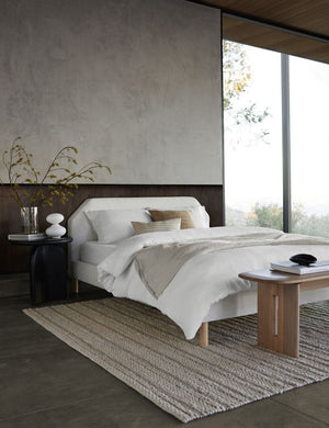 The European Flax Linen white Duvet Set by Cultiver lays on a white linen framed bed in a bedroom with floor to ceiling windows, the black nera nightstand, and a woven cream rug