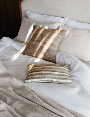 The European Flax Linen white Duvet Set by Cultiver lays on a cream linen and wooden framed bed with brown patterned throw pillows and natural toned linens