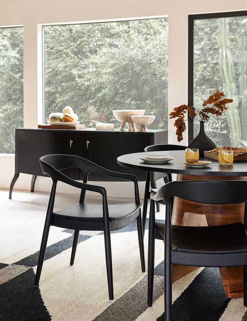 #color::Black | Three Black Ida Dining Arm Chairs sit around a black dining table atop a black, gray, and cream geometric rug