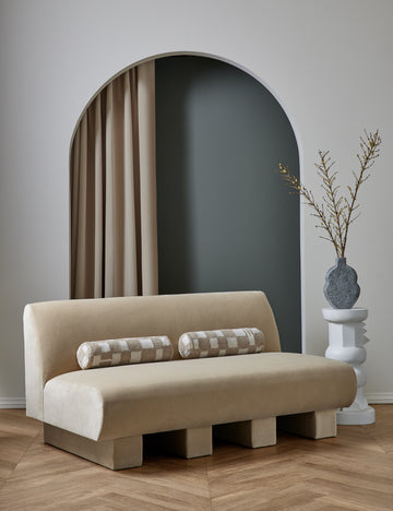 #showall::39840603144291 | The Lena armless brie beige velvet sofa sits in a studio with two checkerboard bolster pillows atop it