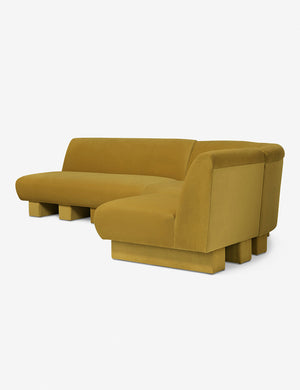 Angled view of the Lena right-facing yellow velvet sectional sofa with upholstered beam legs.