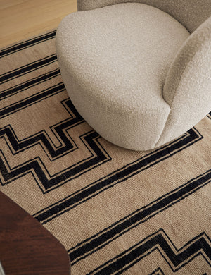 The Senna neutral hand-knotted wool area rug with black geometric pattern sits under a rounded boucle accent chair.