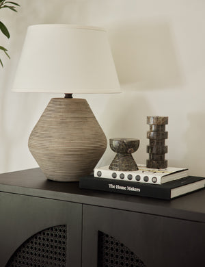 A Khala table lamp with ribbed base and weathered finish sits atop a black side table with black marble sculptural decor and a stack of two books