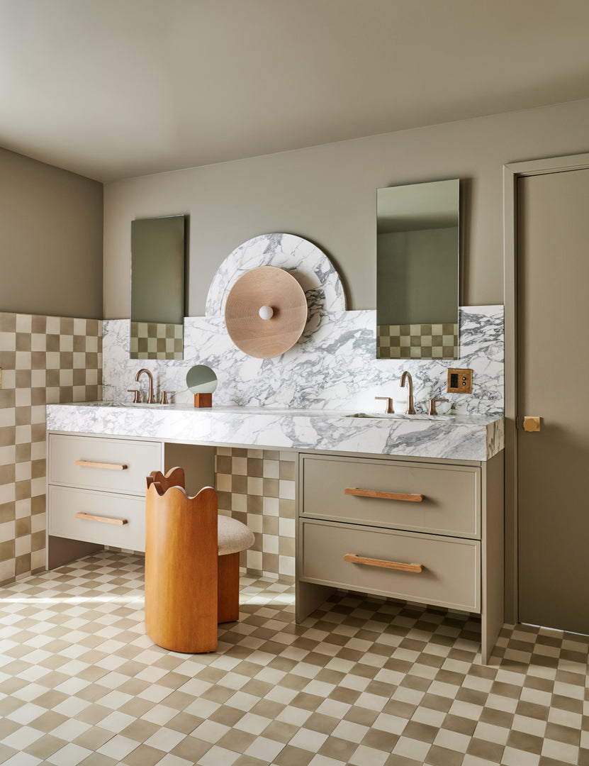 | Ripple Accent Chair sits in a bathroom in between two sinks with a marble counter top and checker-tiled floors and walls