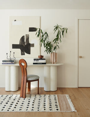 The whit honey wood sculptural dining chair by sarah sherman samuel sits in front of a white console table beneath a black and white abstract wall art.
