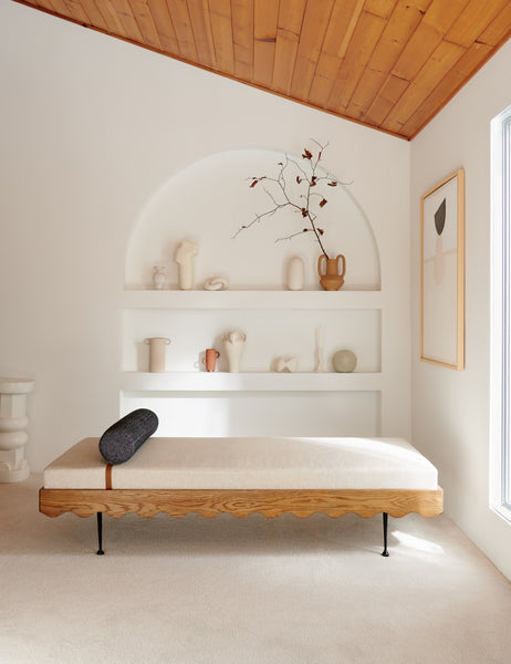 | The Rise Daybed sits in a white room in front of a built-in wall shelf with various decor items 