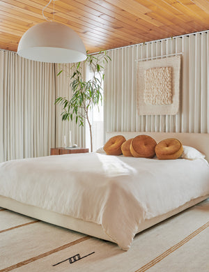 Four Velvet Disc amber Pillows by Sarah Sherman Samuel sit on a cream framed bed on natural linens in a bedroom with curtained walls