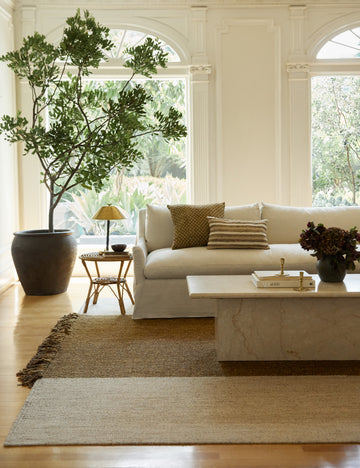 #size::2-6--x-8- #size::6--x-9- #size::8--x-10- #size::9--x-12- #size::10--x-14- #size::12--x-15- | The wilcox rug sits underneath a natural linen slipcover sofa and a rattan cane side table with a brass lamp