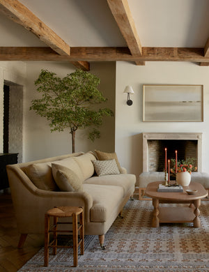 The Rivington brie beige velvet sofa sits atop a patterned rug behind an oval coffee table under wooden beamed ceilings