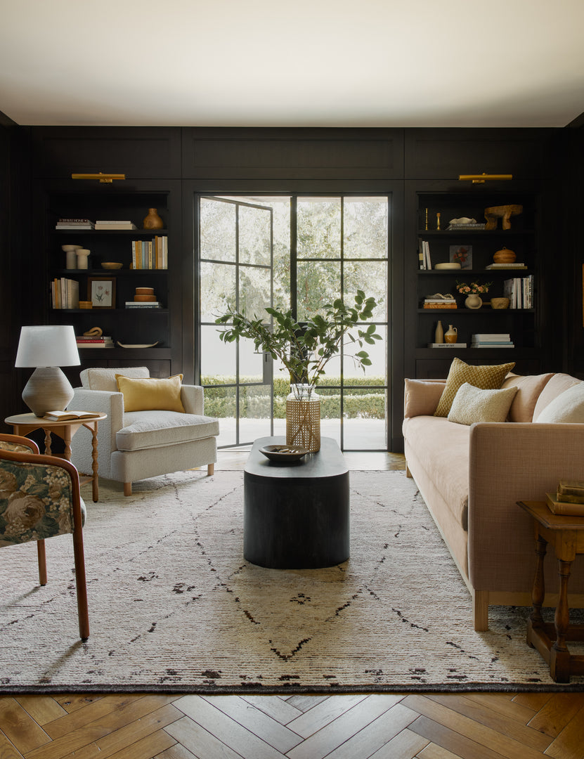 | The Rosanne rug lays in a living room with black walls under a natural-toned sofa, a black coffee table,and two accent chairs