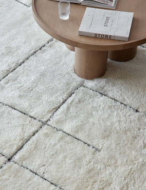 The costa rug lays under a round wooden coffee table with cylindrical legs and a glass and a book sitting atop it
