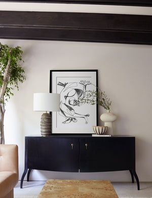 The Stretch Print in a black frame sits on a black sideboard next to a sculptural vase and a ribbed lamp