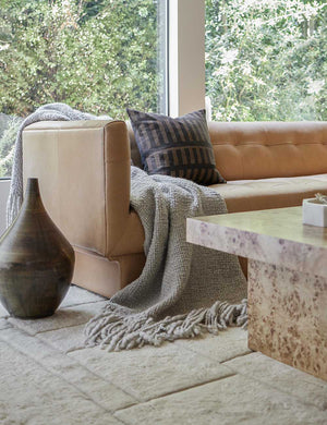 The Goleta gray chunky wool knit throw blanket with tasseled ends lays on a light brown leather sofa in a living room