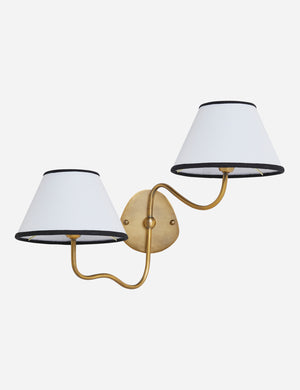 Magdalene brass double sconce with a white linen shade that has a black trim, a round wall mount, and an arched arm