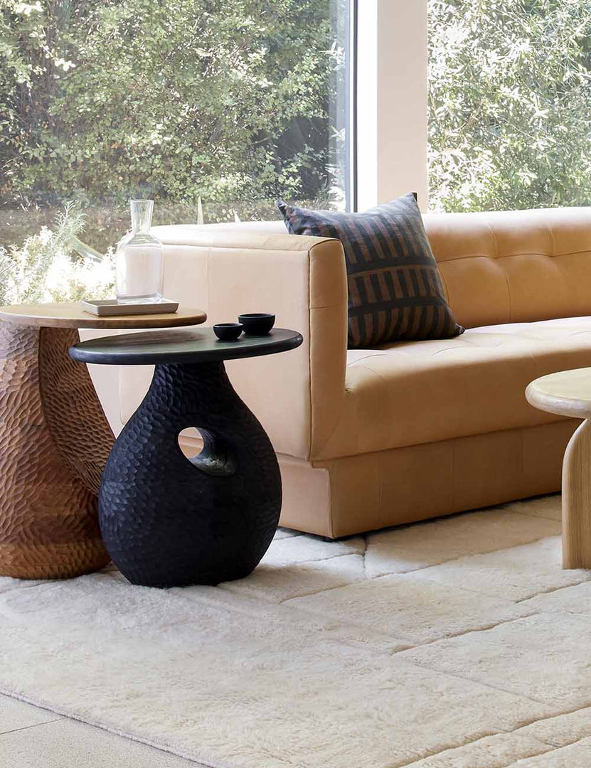 | Corso black mango wood side table is nested under a natural wooden side table atop a plush cream rug and next to a leather sofa