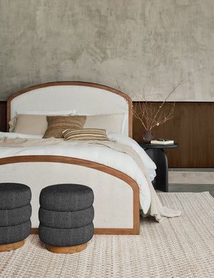 The Crawford natural linen platform bed sits atop a natural-toned rug next to a black nightstand with two ottomans
