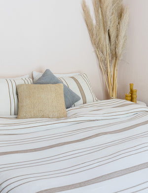 The Marlo Cotton hand loomed beige striped Duvet Set by House No. 23 lays on a bed with natural and gray throw pillows in a bedroom