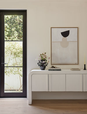 A Foothold Print by Sarah Sherman Samuel is hung on a cream wall above a white sideboard with books and a black vase