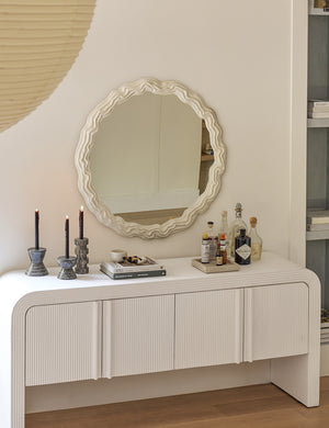 The anastasia round mirror hangs above a white sideboard above a bar set, marble candles, and a stack of books